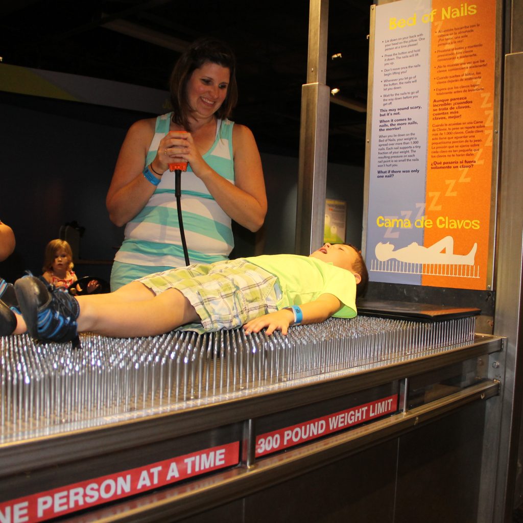 Cohen laying on a bed of nails at a science center