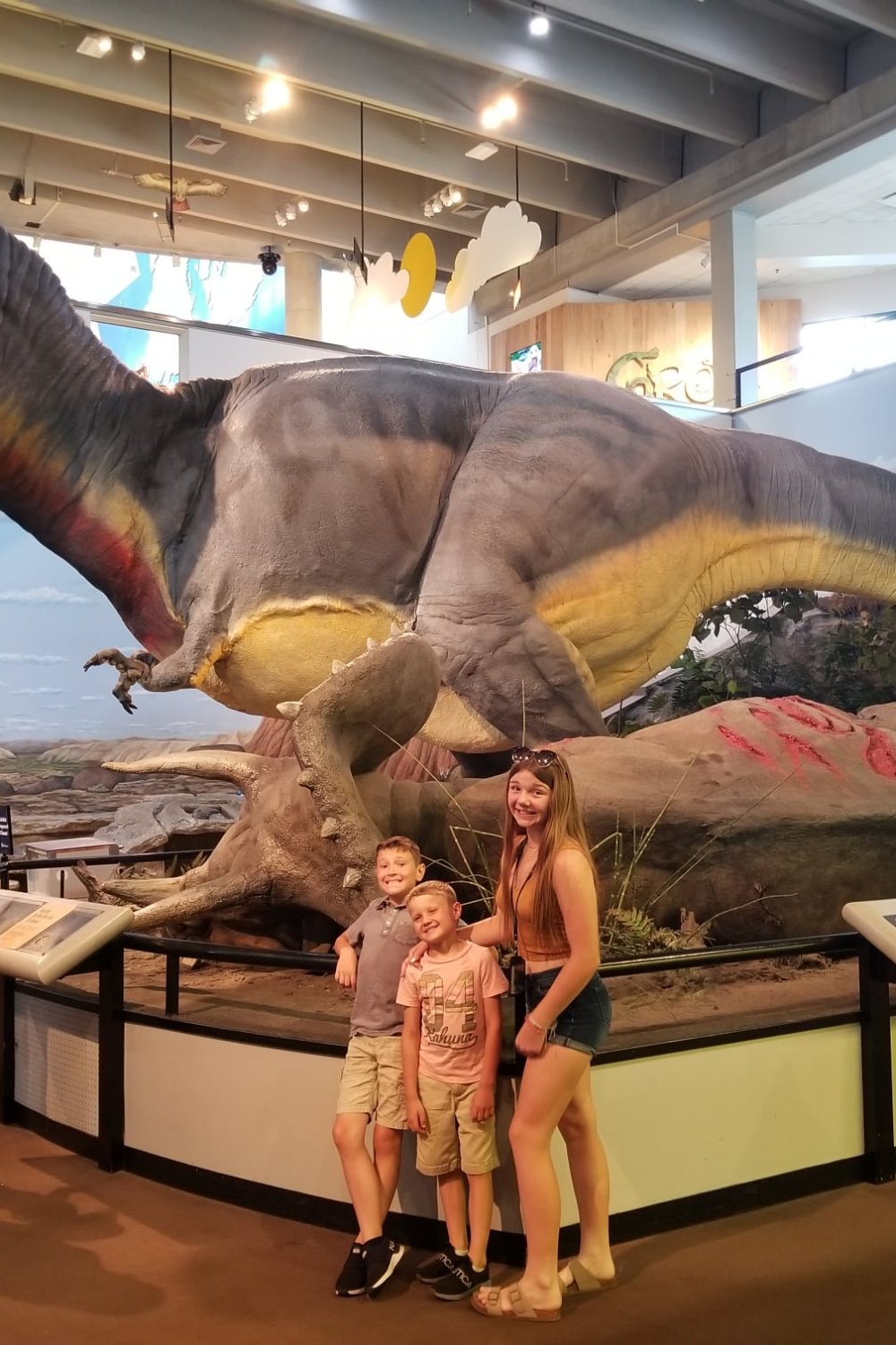 Kids posing in fronf ot the dinosuar at the St. Louis Science Center whiile checking out unique road trip stops in the midwest